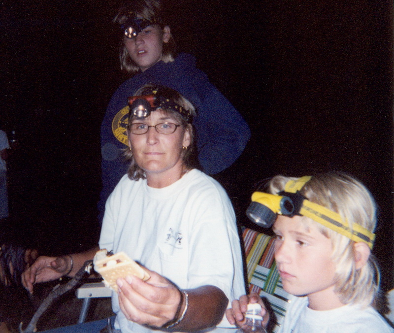 Adults and kids making s'mores by headlamp at night